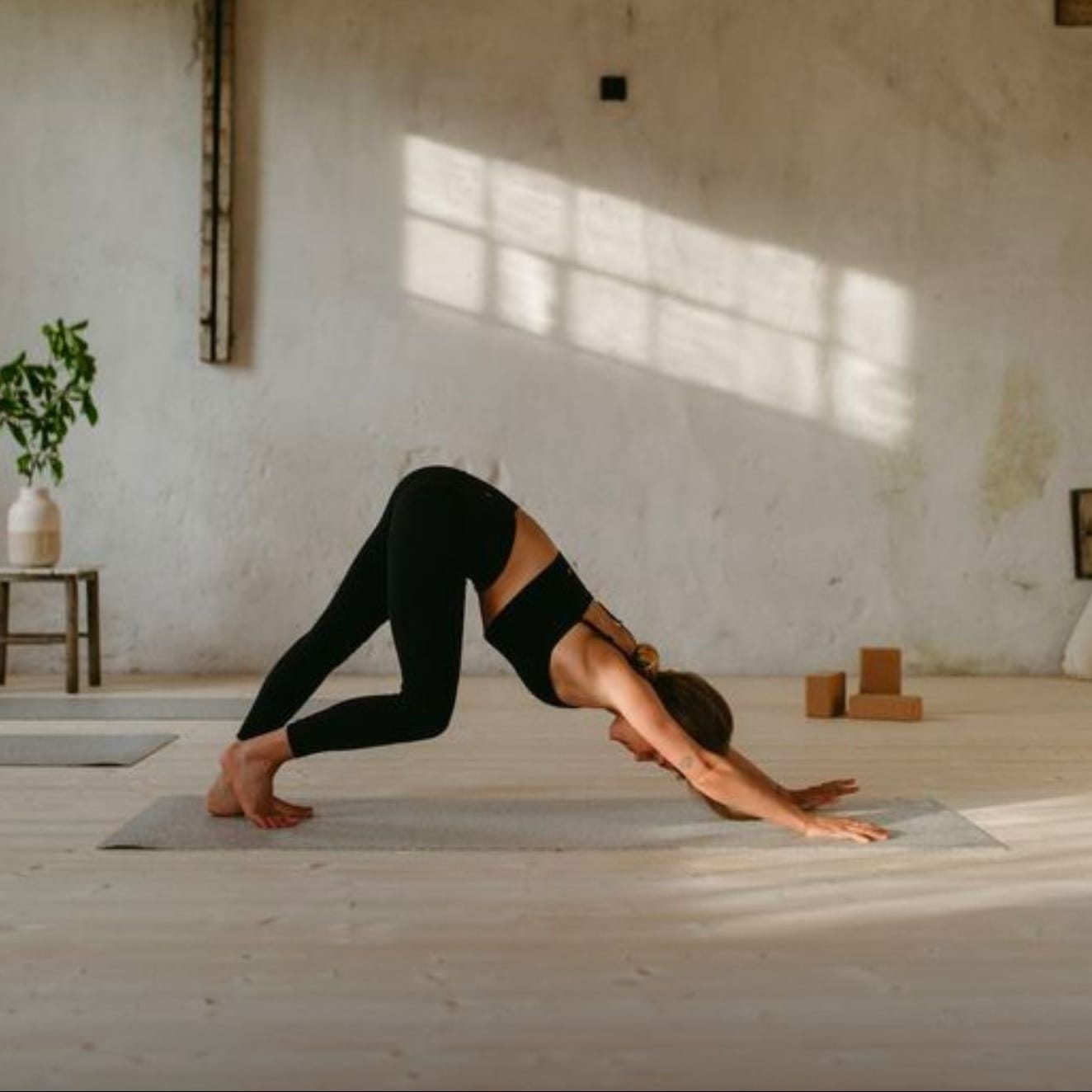 Person practicing yoga in a sunlit room with wooden floors and white walls.