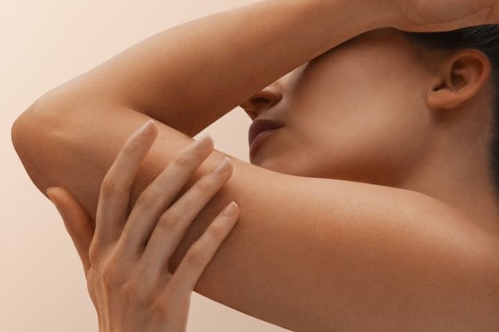 Clean, glowing skin with one arm raised, touching their face against a beige background